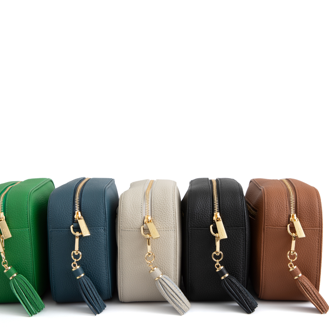 Five small leather bags in green, blue, beige, black, and brown with gold zippers and tassels on a white background.