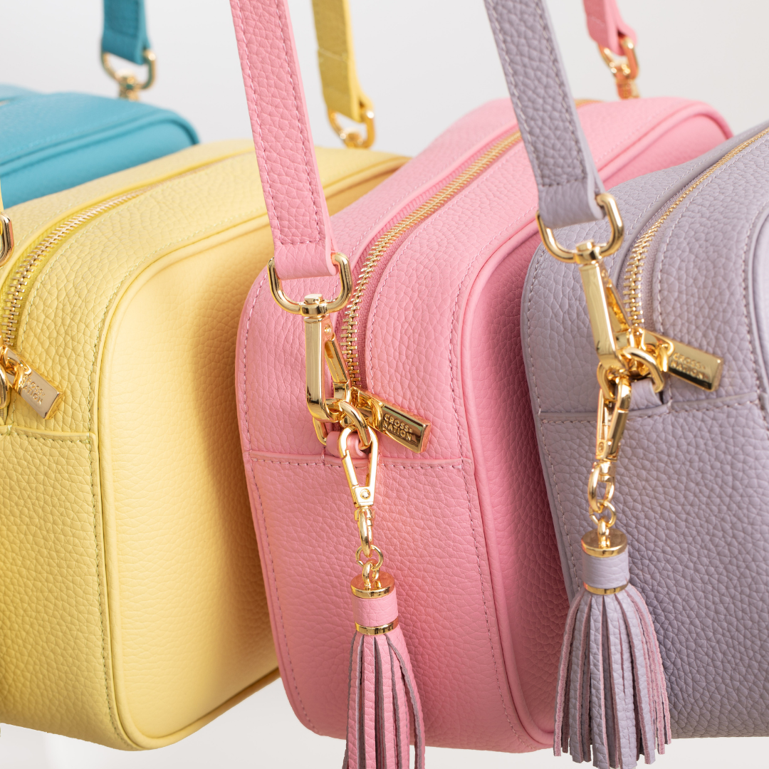 Three handbags in yellow, pink, and gray with matching tassel keychains on a light background.
