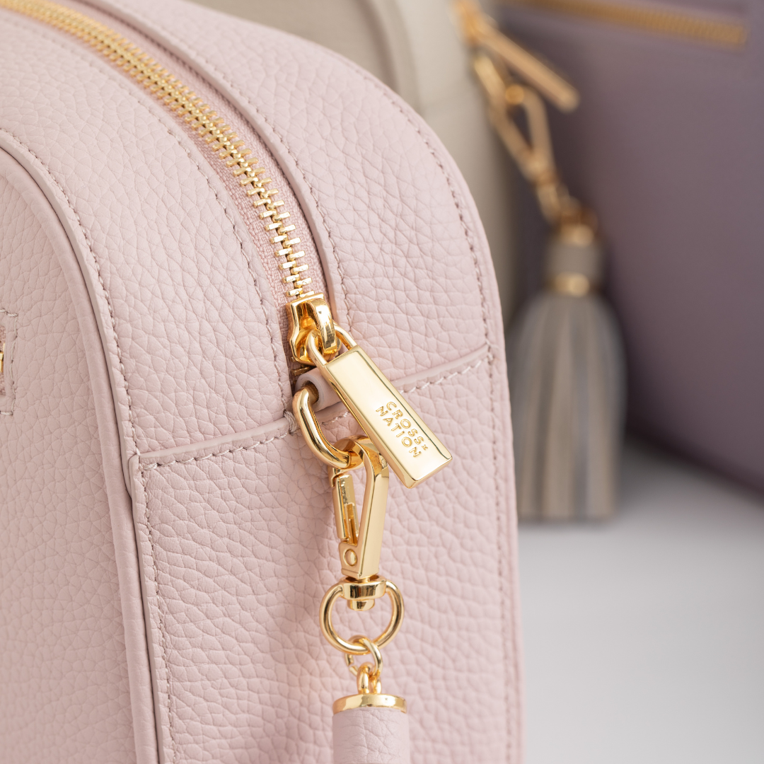 Close-up of a pink handbag with a gold zipper and tag, featuring the brand name Cross Nation