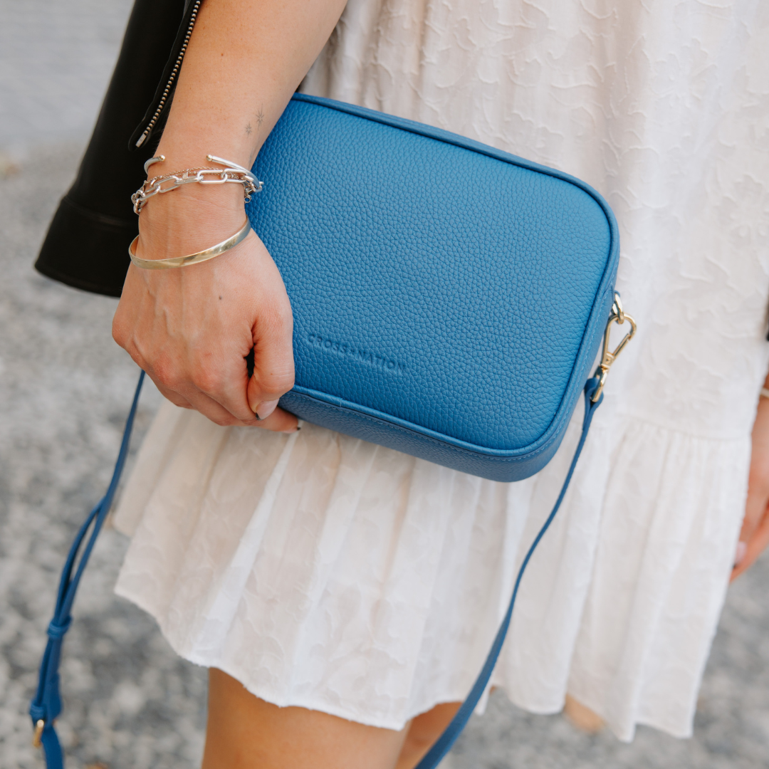 Person holding a blue crossbody bag with 'Cross nation' branding.