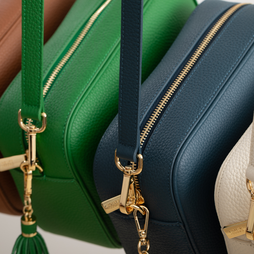 Close-up of green, blue, and beige handbags with gold zippers and tassels.