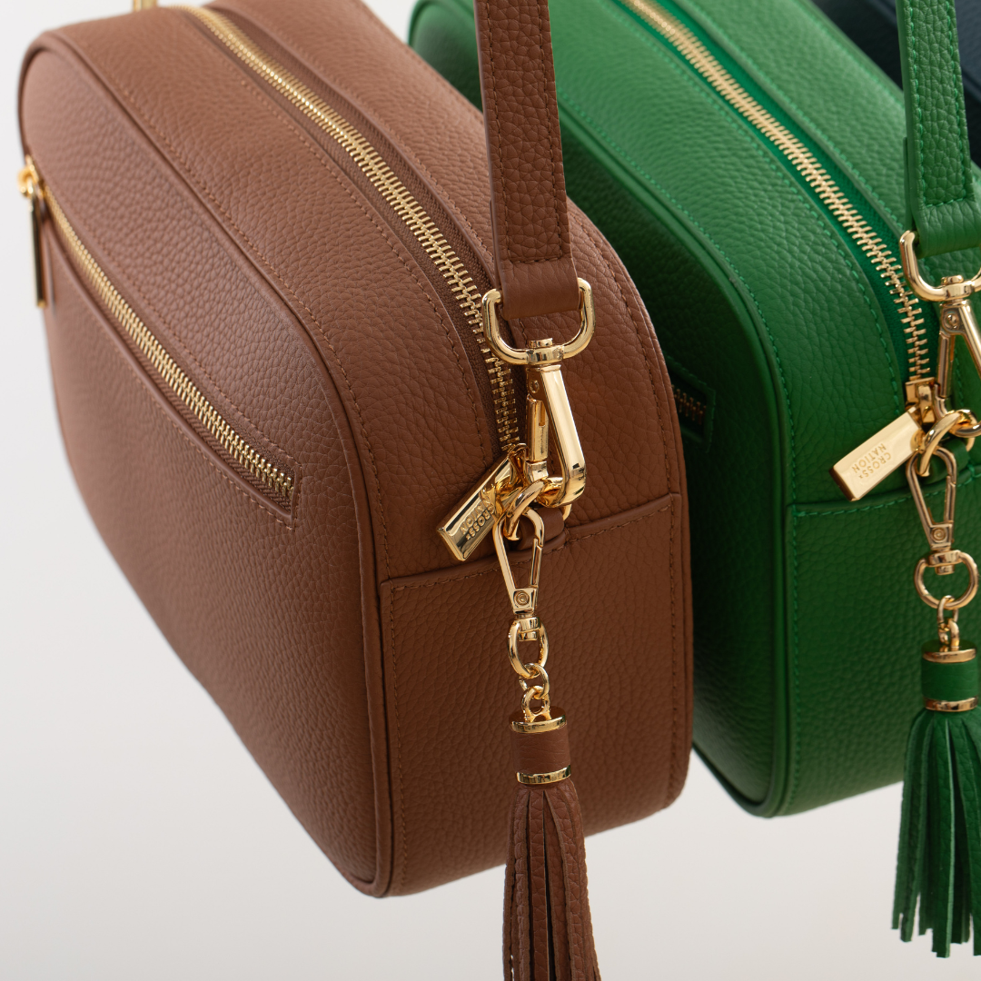 Brown and green leather crossbody bags with gold zippers and tassels on a light gray background