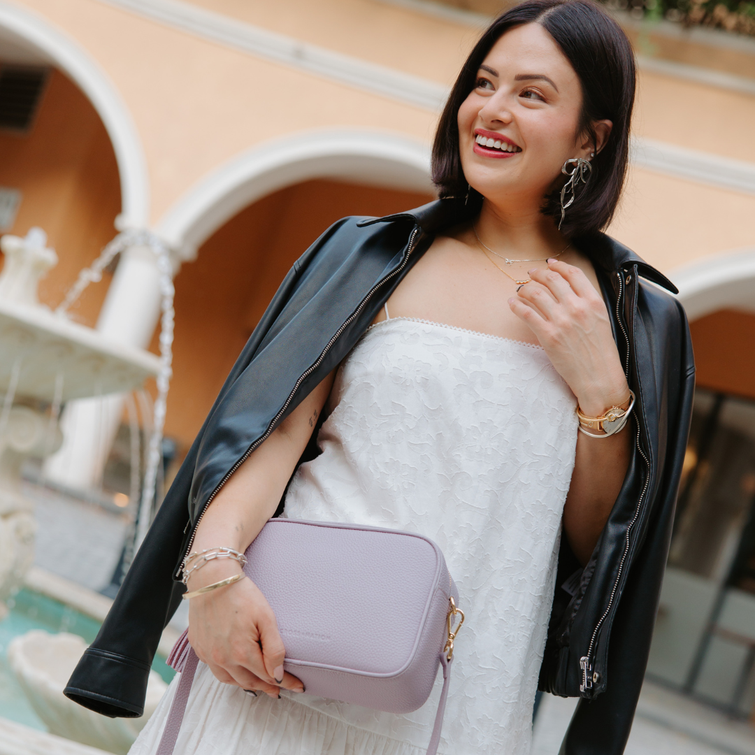 Woman holding a purple handbag in an outdoor setting with architectural elements.
