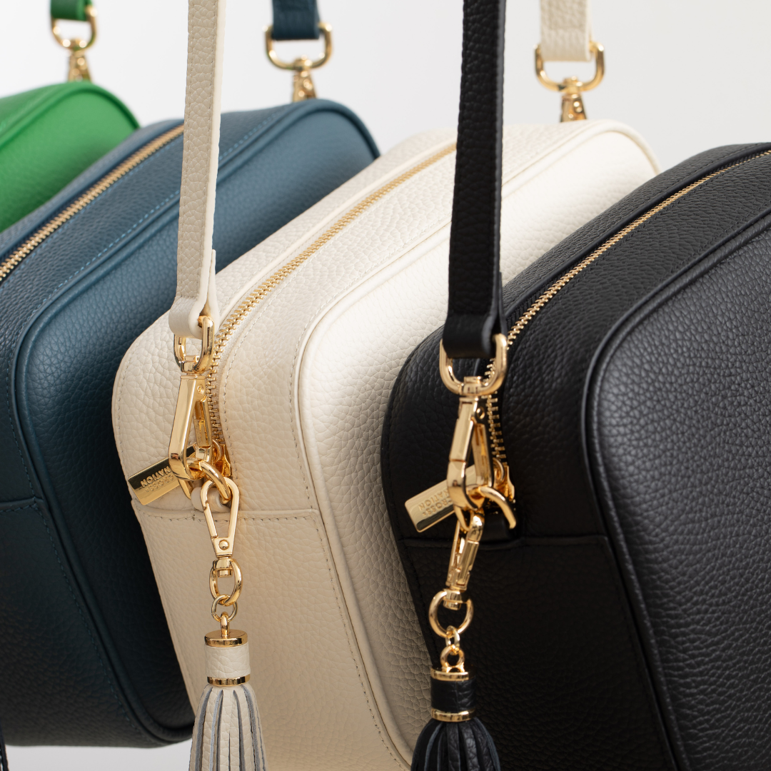 Four leather crossbody handbags in green, blue, beige, and black with gold zipper pulls and tassels.