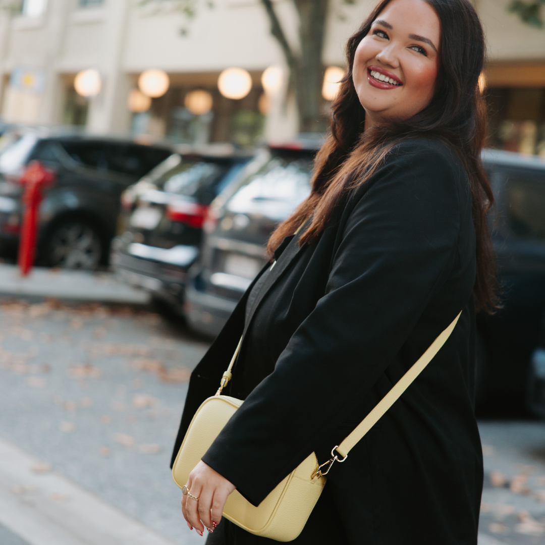 Woman in a black coat with a yellow leather crossbody bag standing on a street.