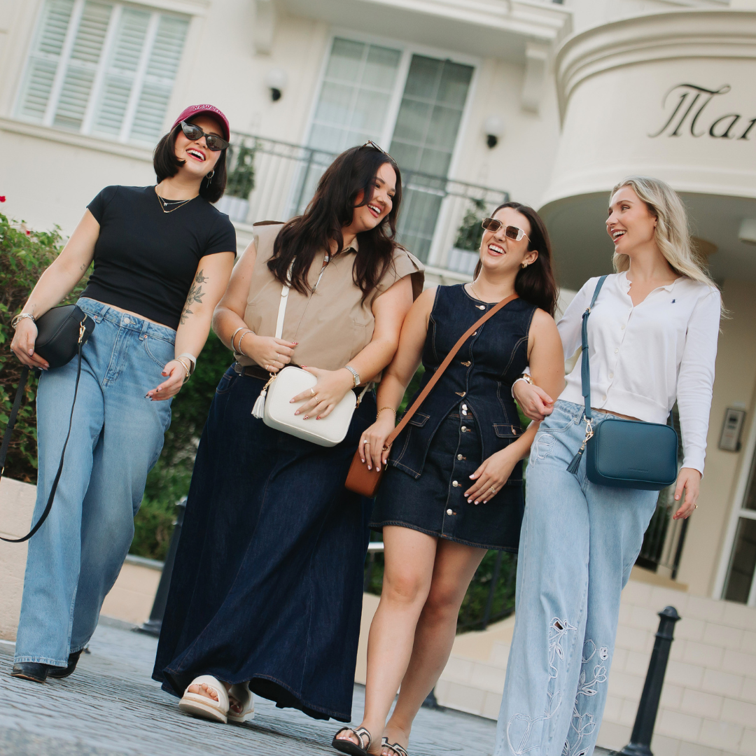 Four women walking together in front of a building with 'Man' on it wearing crossbody bags.