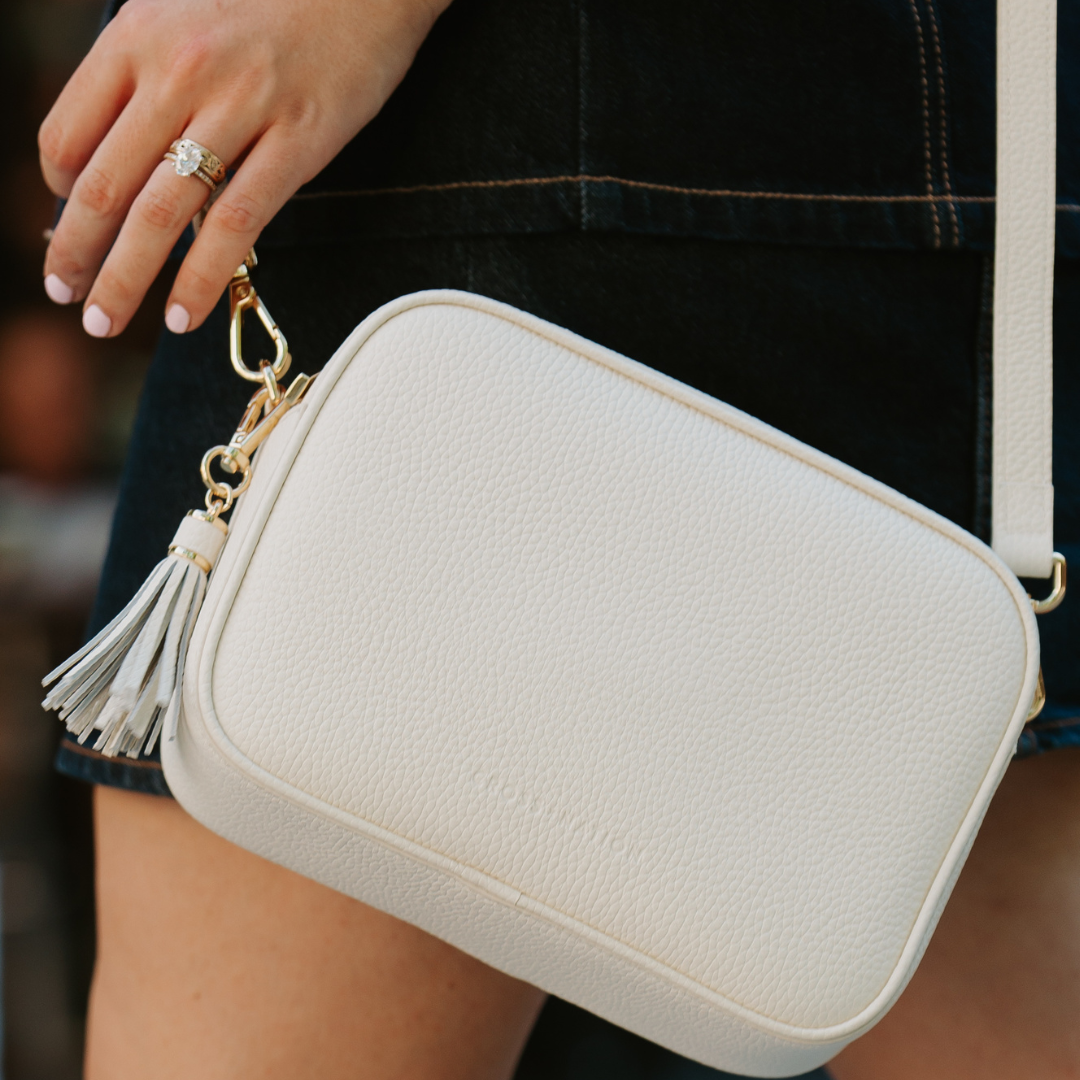 White handbag with a tassel detail held by a person wearing a ring.