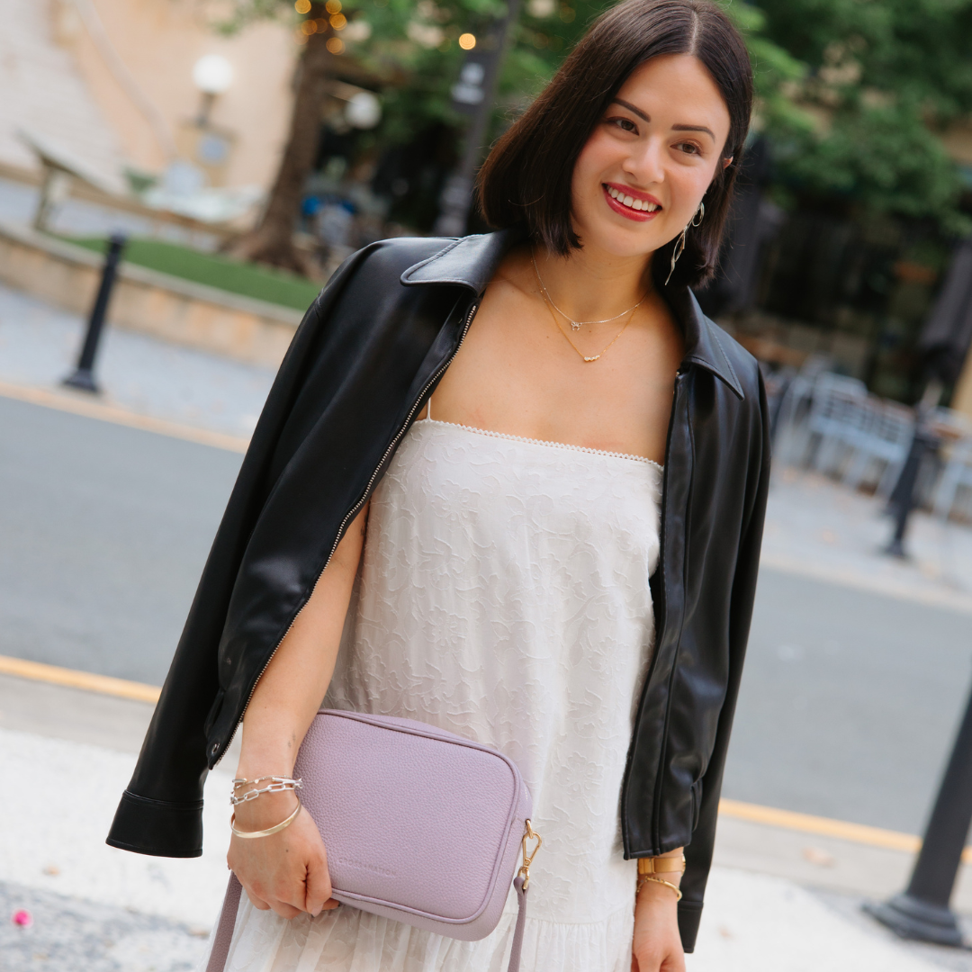 Woman in a light dress with a black leather jacket and purple handbag on a city street.