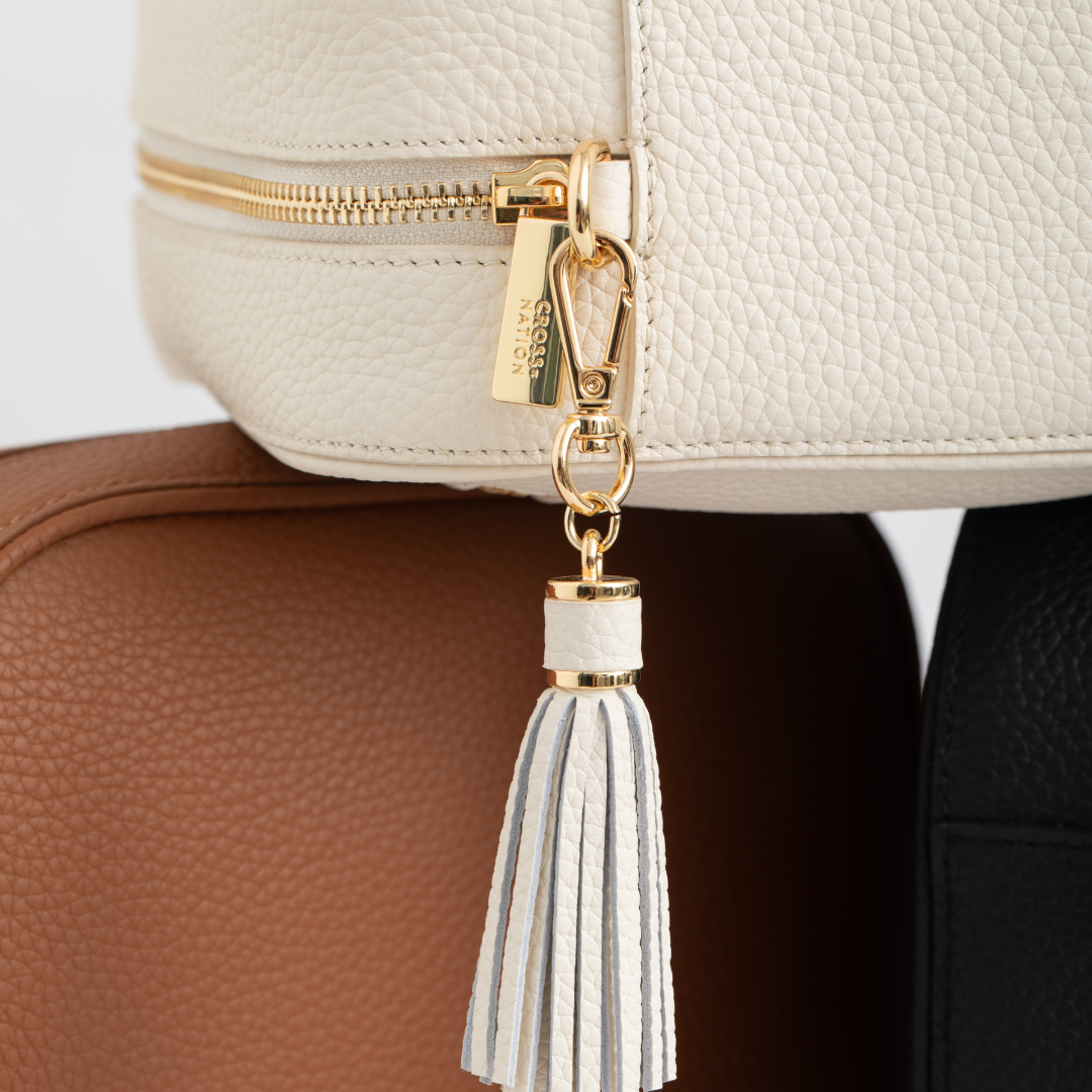 Close-up of a beige handbag with a gold zipper and white tassel detail.