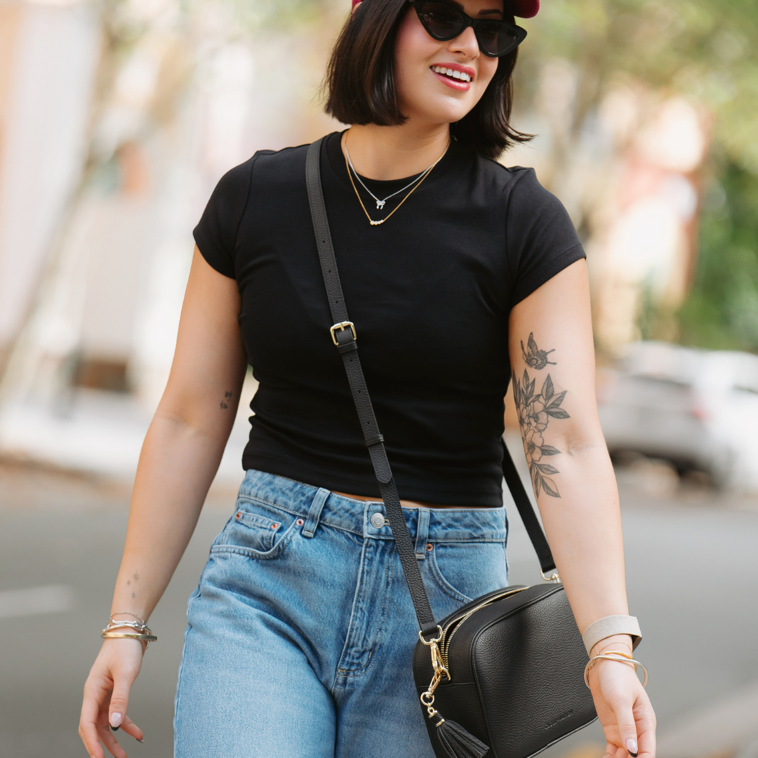 woman wearing a black leather crossbody bag, black t-shirt and blue jeans with sunglasses
