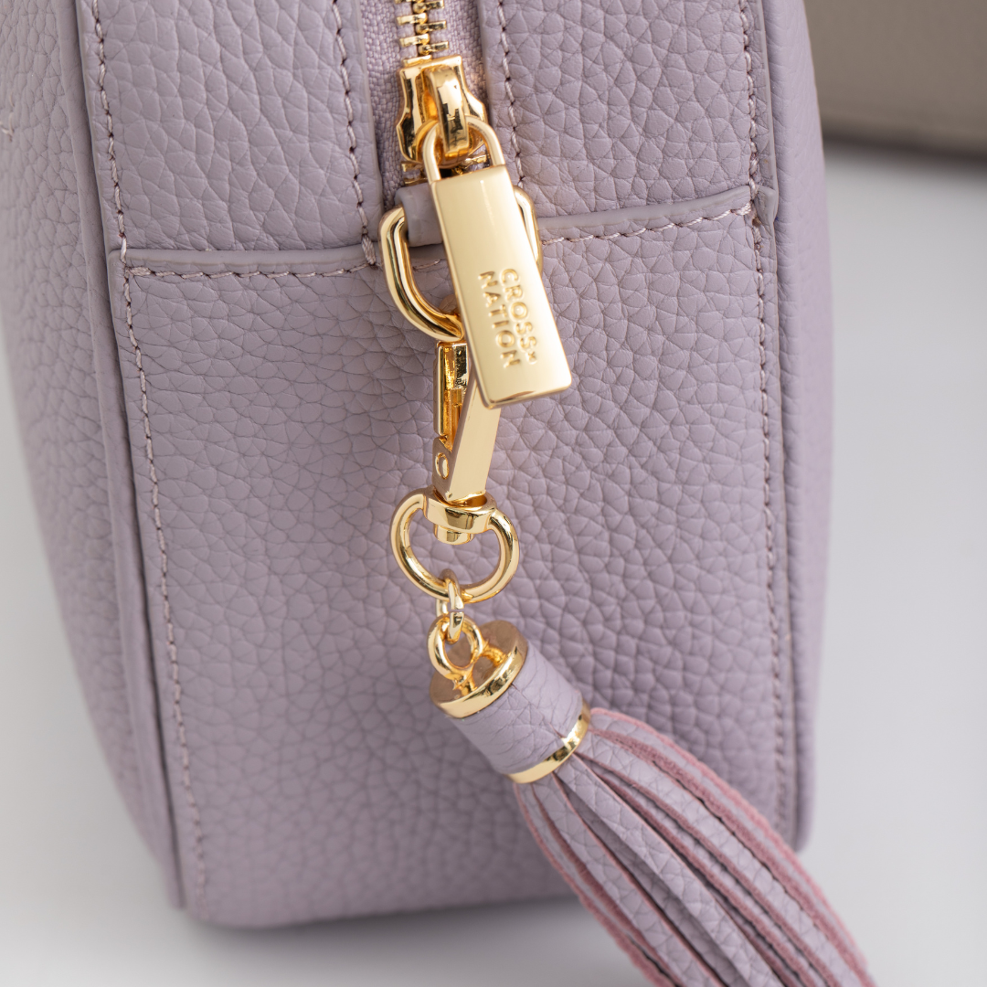 Purple handbag with gold zipper and tassel detail on a light gray background