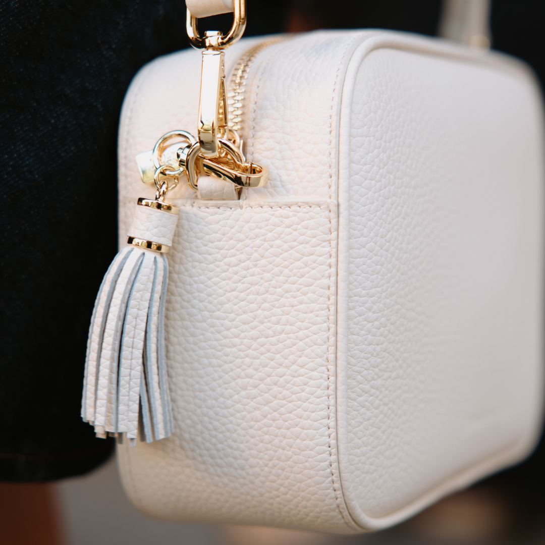 White textured handbag with a gold zipper and tassel detail on a blurred background