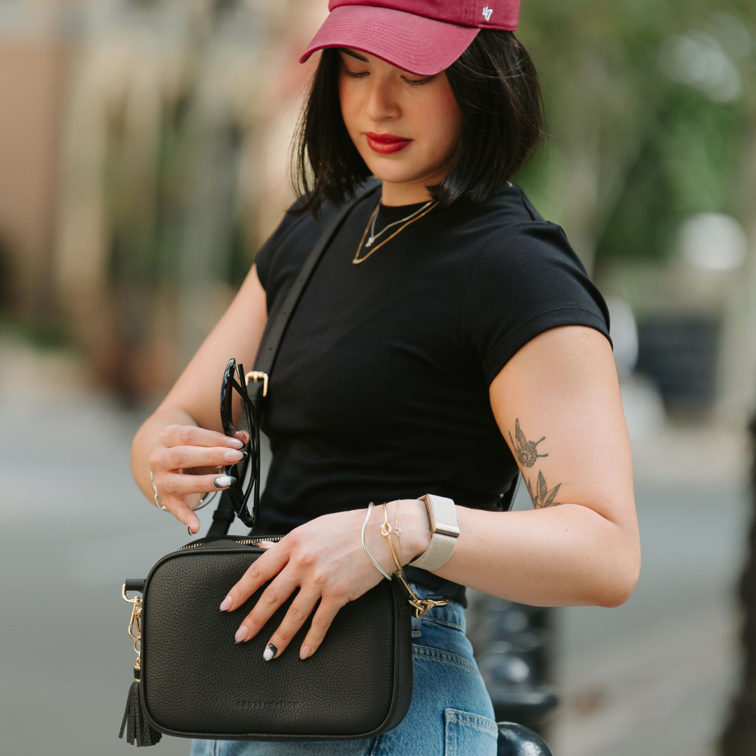 Woman holding a black handbag wearing a pink cap and black top outdoors